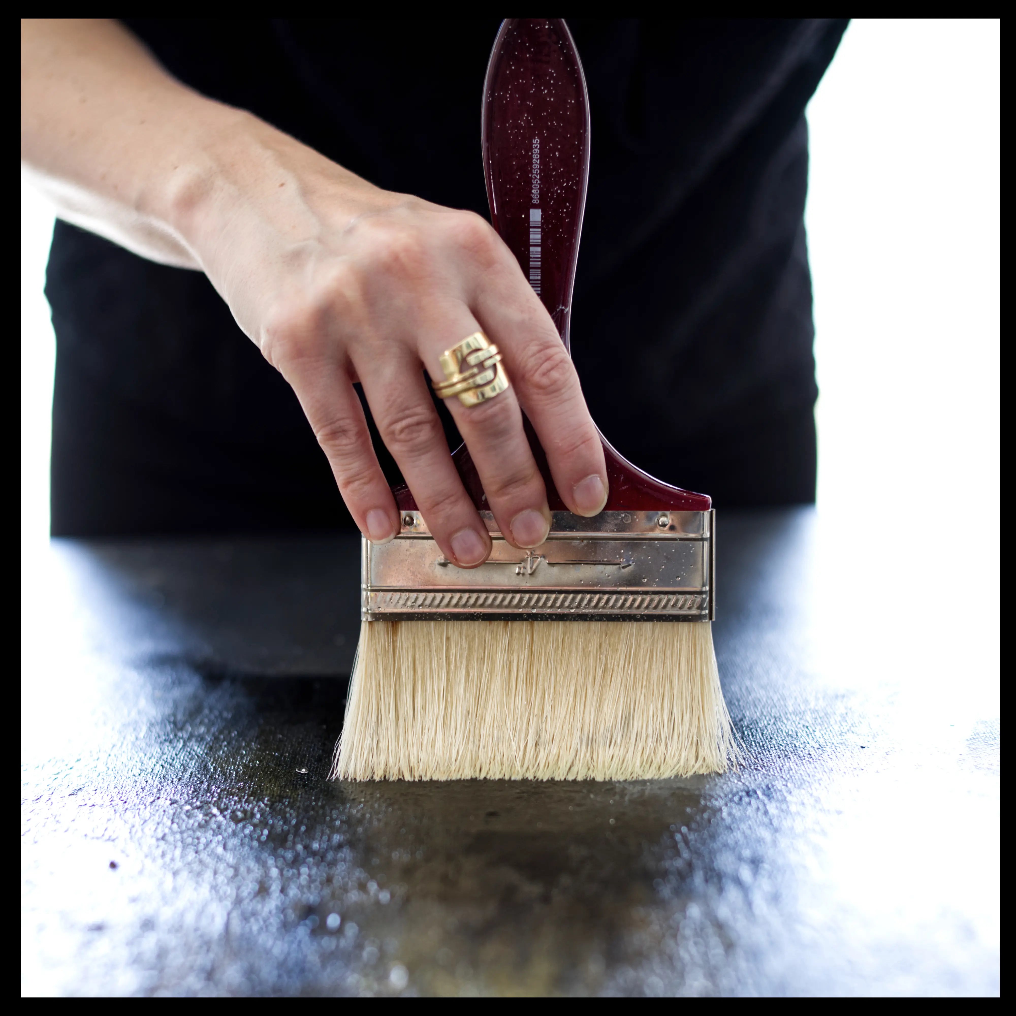 Close up on Anez Ka's hand and a large brush while painting an abstract artwork in the artist studio.